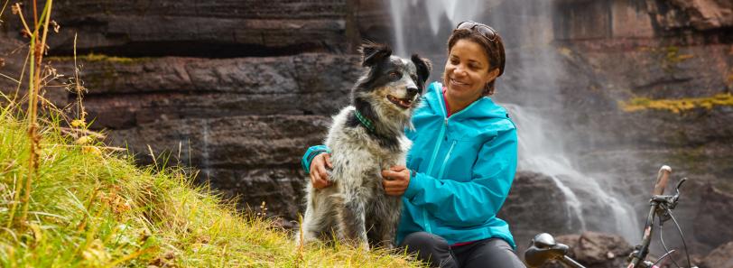 woman petting dog in front of waterfall