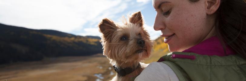 Woman holding a mini dog in front of a river. 