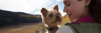 Woman holding a mini dog in front of a river. 