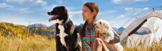 Woman sitting with two dogs at a campsite 
