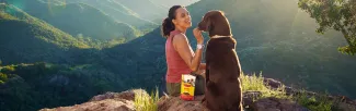 Woman feeding dog Zuke&#039;s treats on a hike
