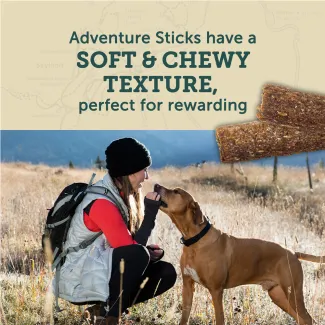 Woman kneeling to reward her dog with a Zukes Adventure Stick with text, soft and chewy texture, perfect for rewarding.